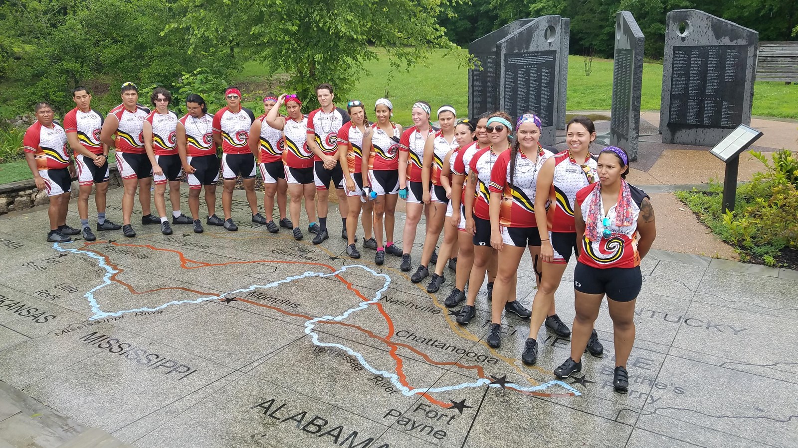 Group of people standing on a ground map of the Trail of Tears with memorial behind.