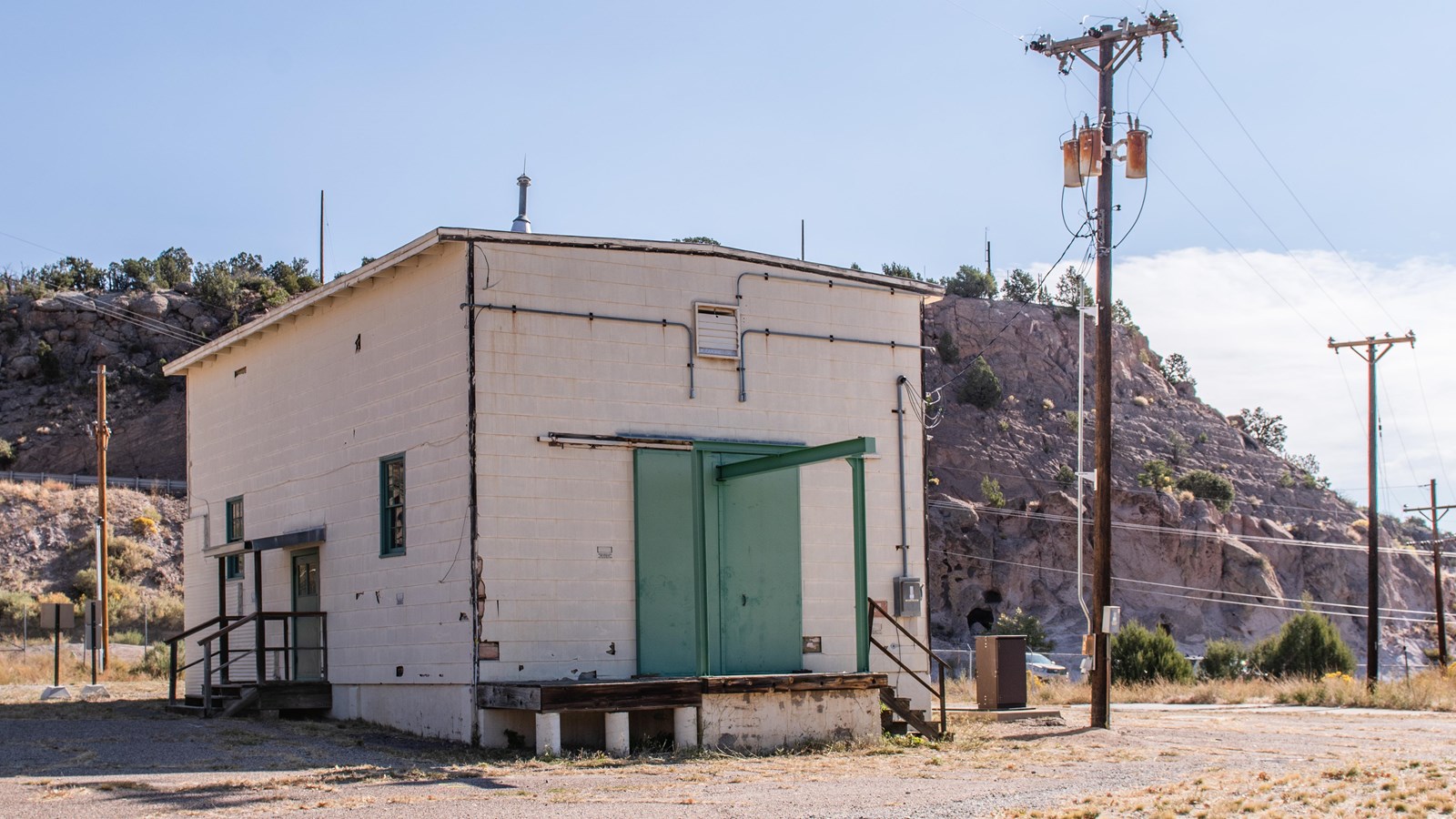 A white-sided building with a green door sits on paved ground.