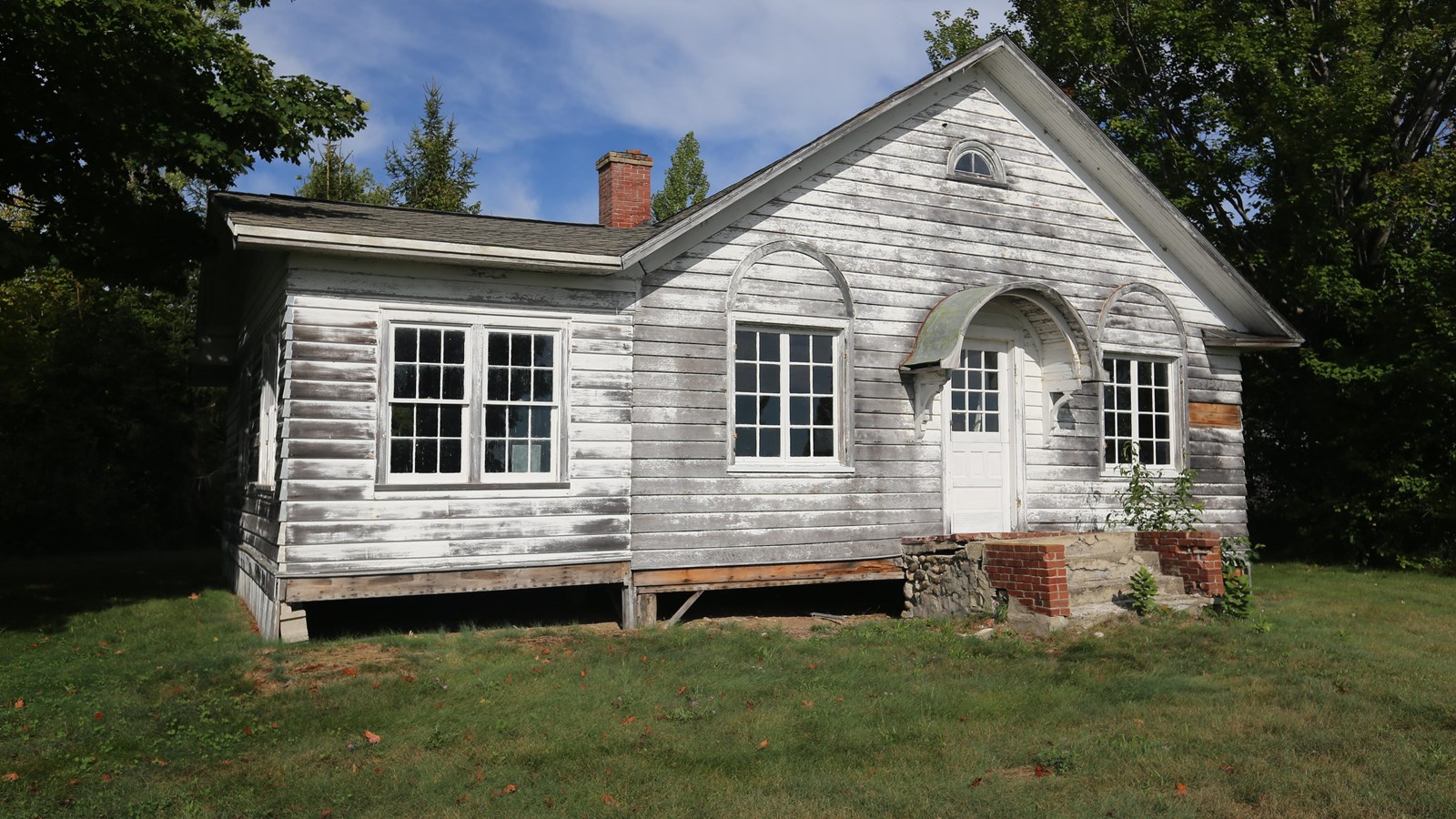 White, clapboard house with graying paint and small arches over front porch and windows