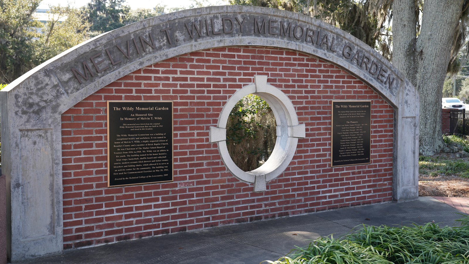 A brick arch with a porthole window and brass plaques.
