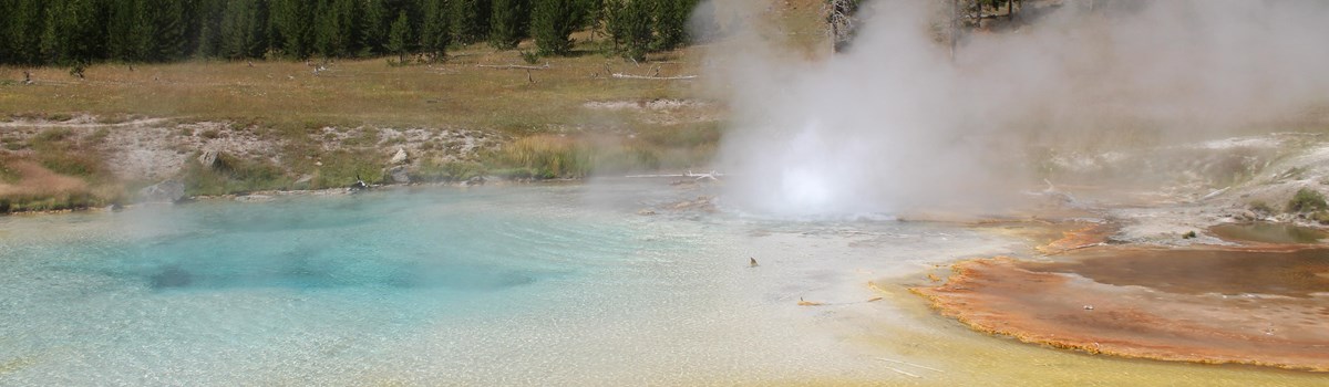 Steam rises from a blue-, yellow-, and orange-colored hot spring.
