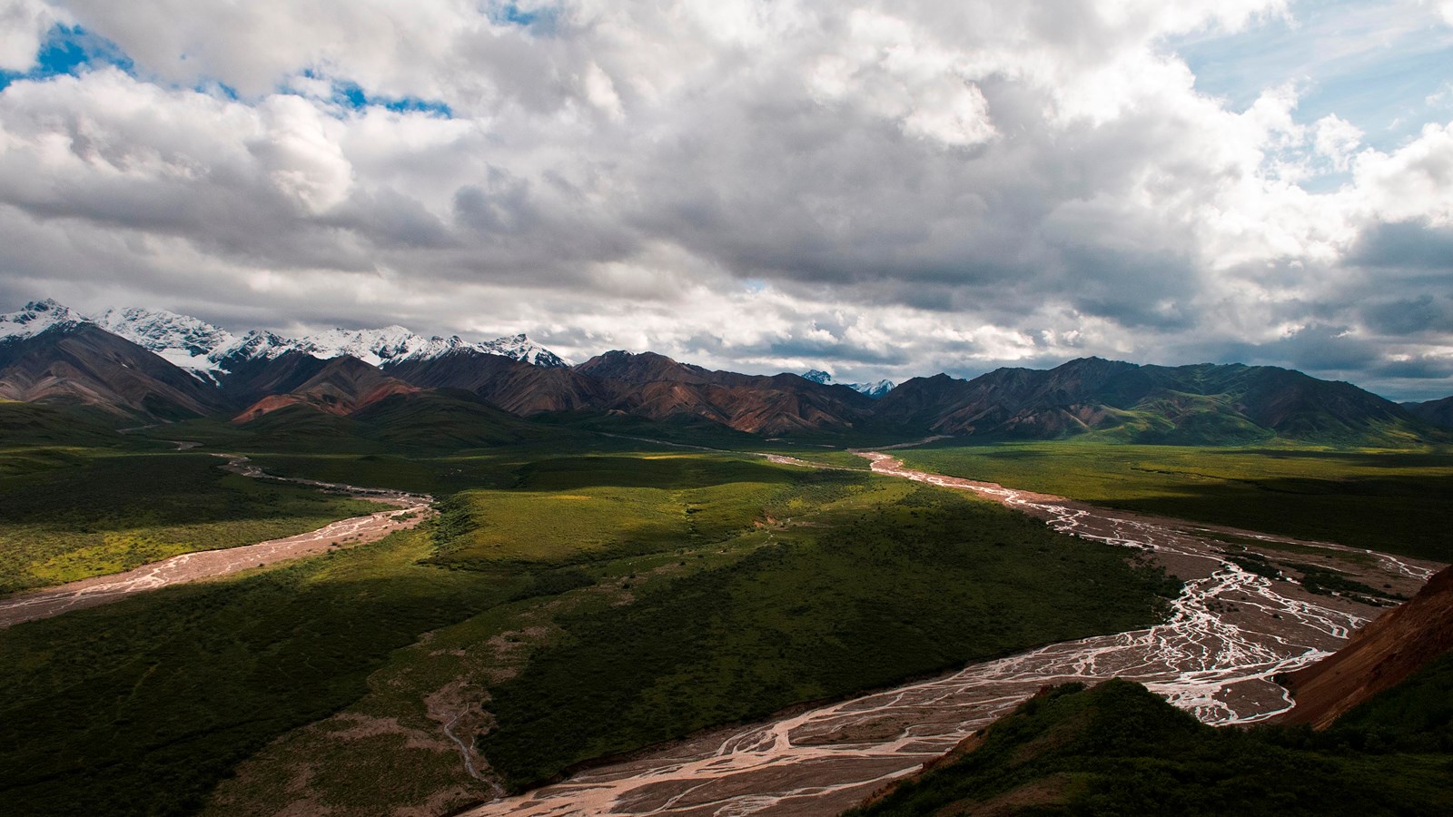 a landscape of rivers and shrubs leading up to distant mountains