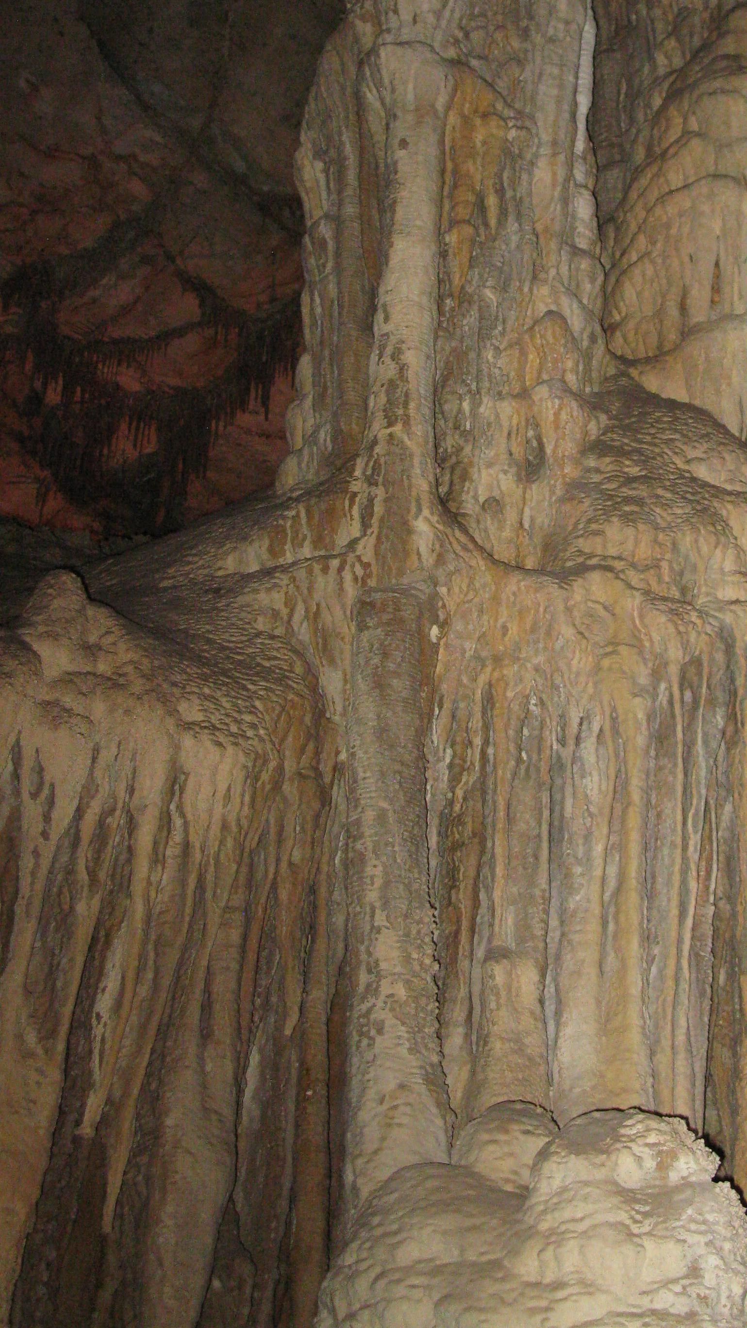 Tan, drippy looking cave formations hang from a wall, with many different textures and angles.