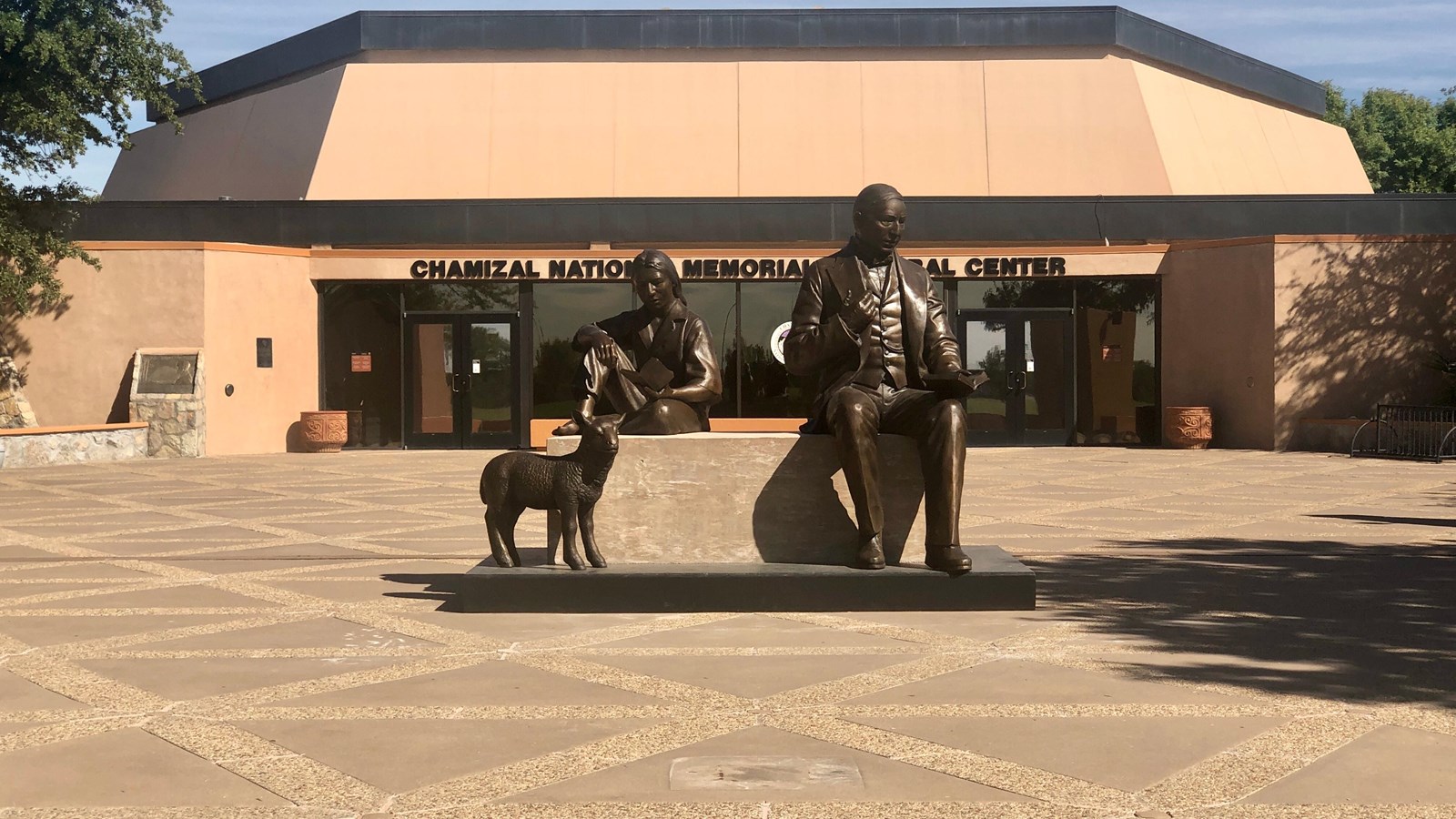 Larger than life sculpture is on open, paved esplanade in front of cultural center