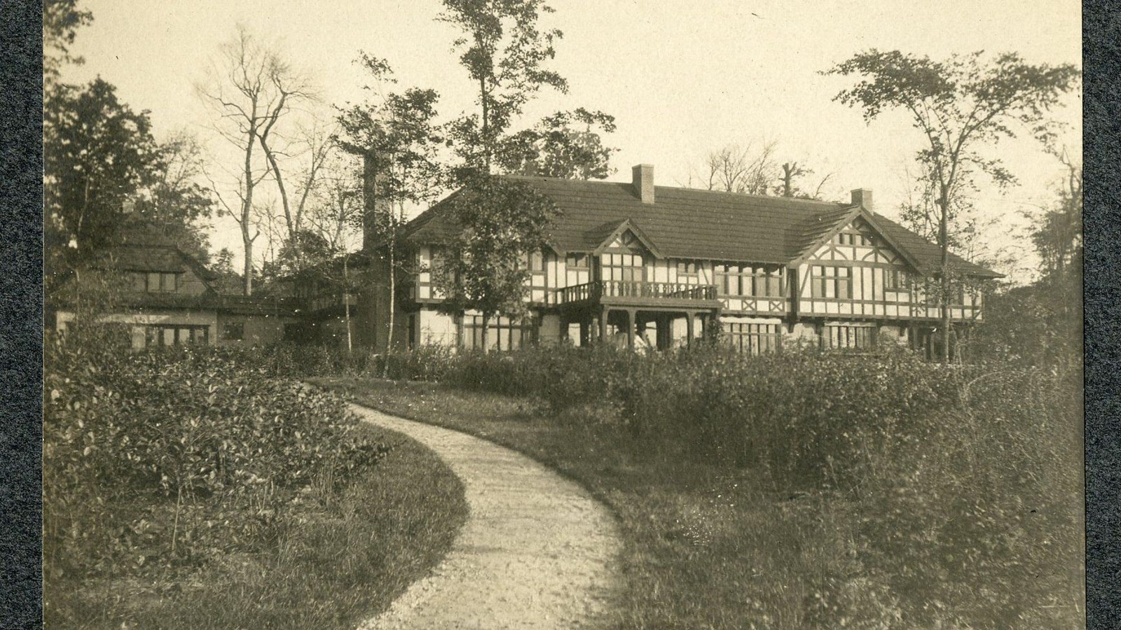 Black and white of dirt path cutting through grassy area leading to house. 