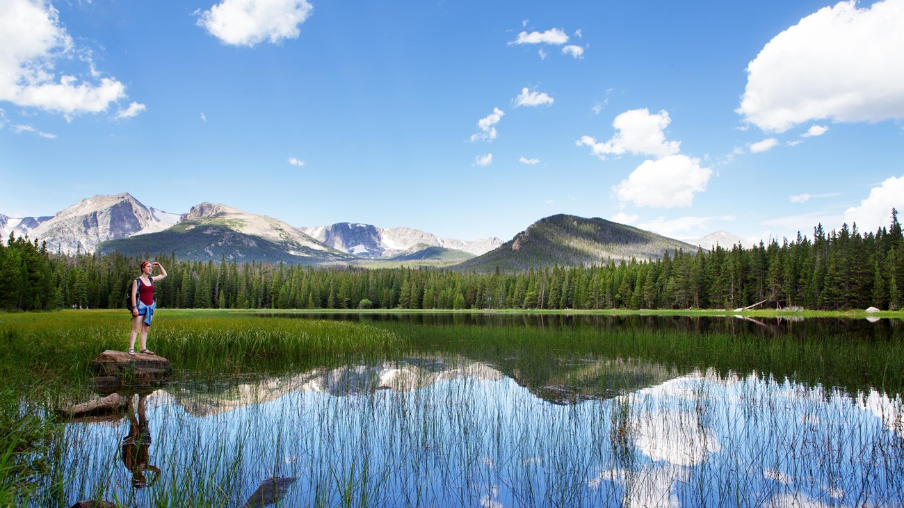 a woman stands on a rock looking out over a lake