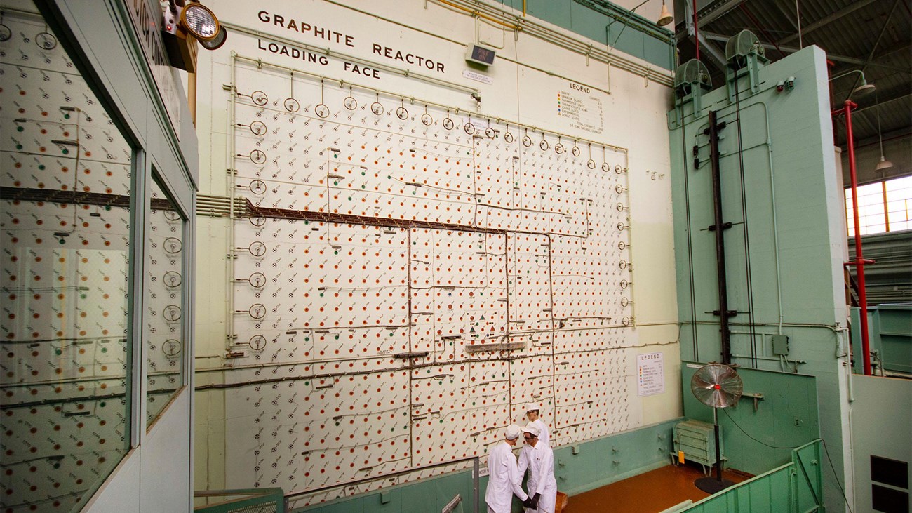 A large industrial wall with several holes and three mannequins at the base of the wall