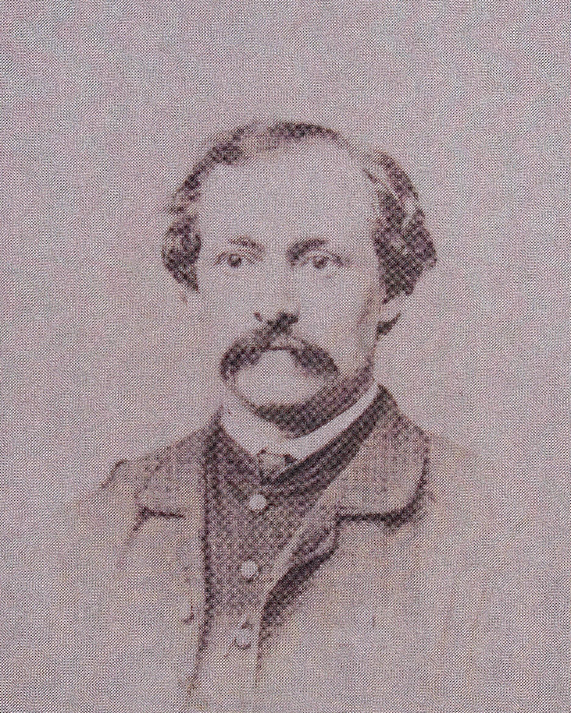 An 1800s portrait photo depicts the bust of a mustached man in a collared shirt, vest, and jacket. 