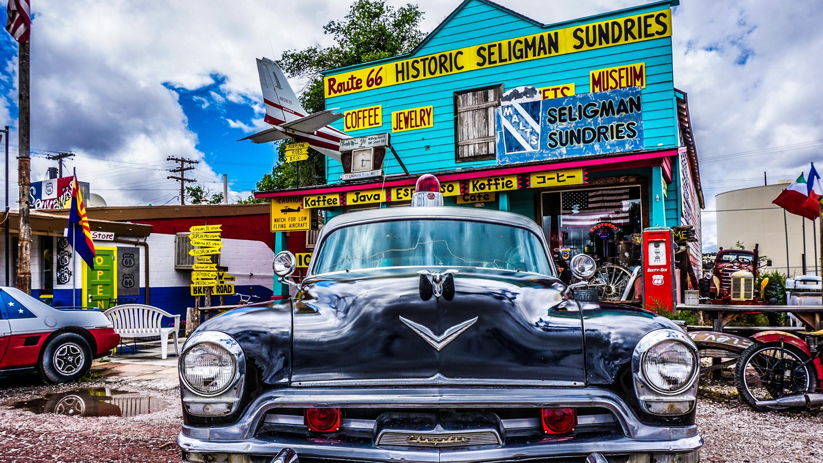 A two story turquoise blue building with yellow and black signs. Out front are old-fashioned cars.