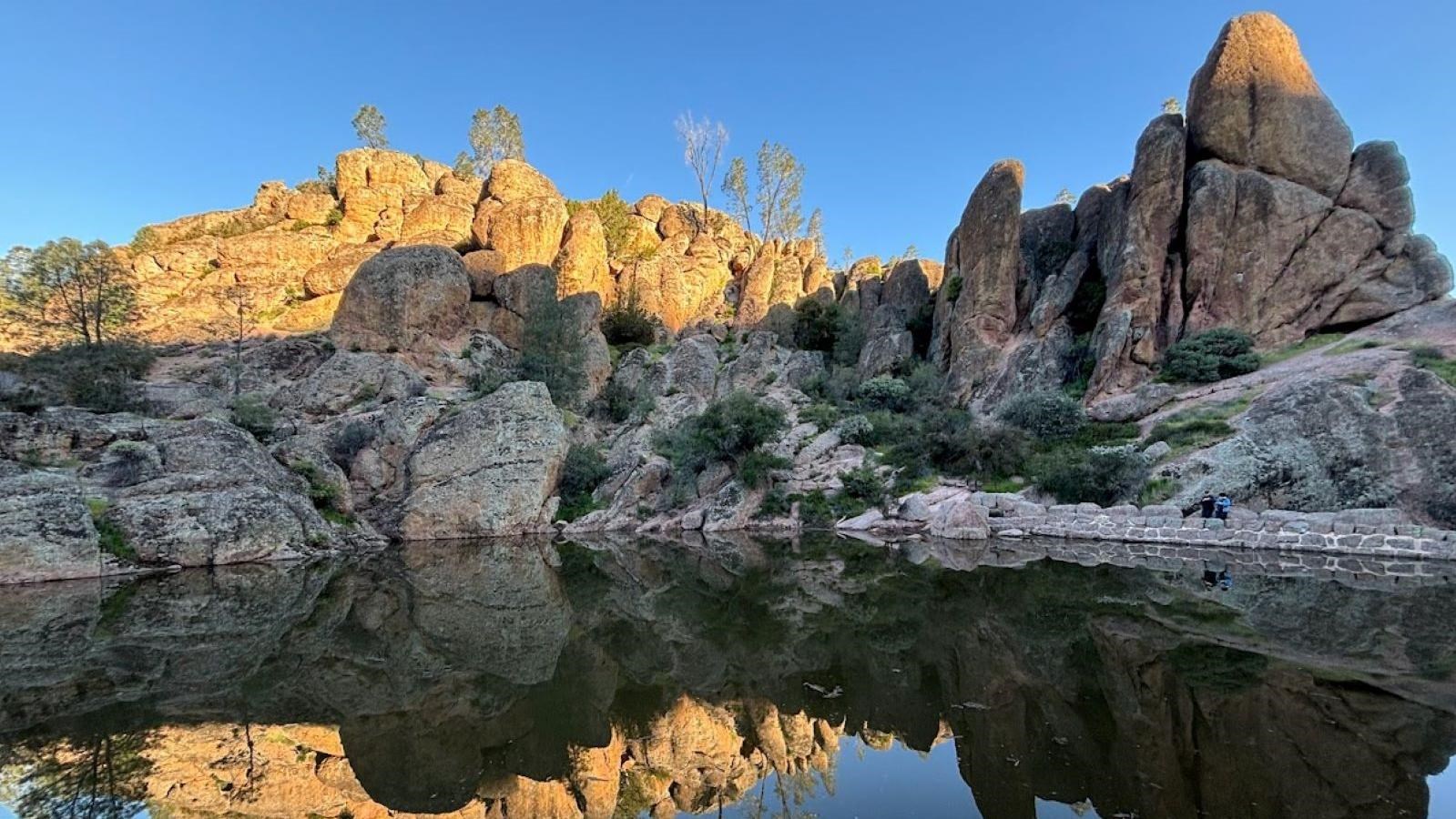 Steep rocks next to a stone dam and reservoir reflecting the rocks