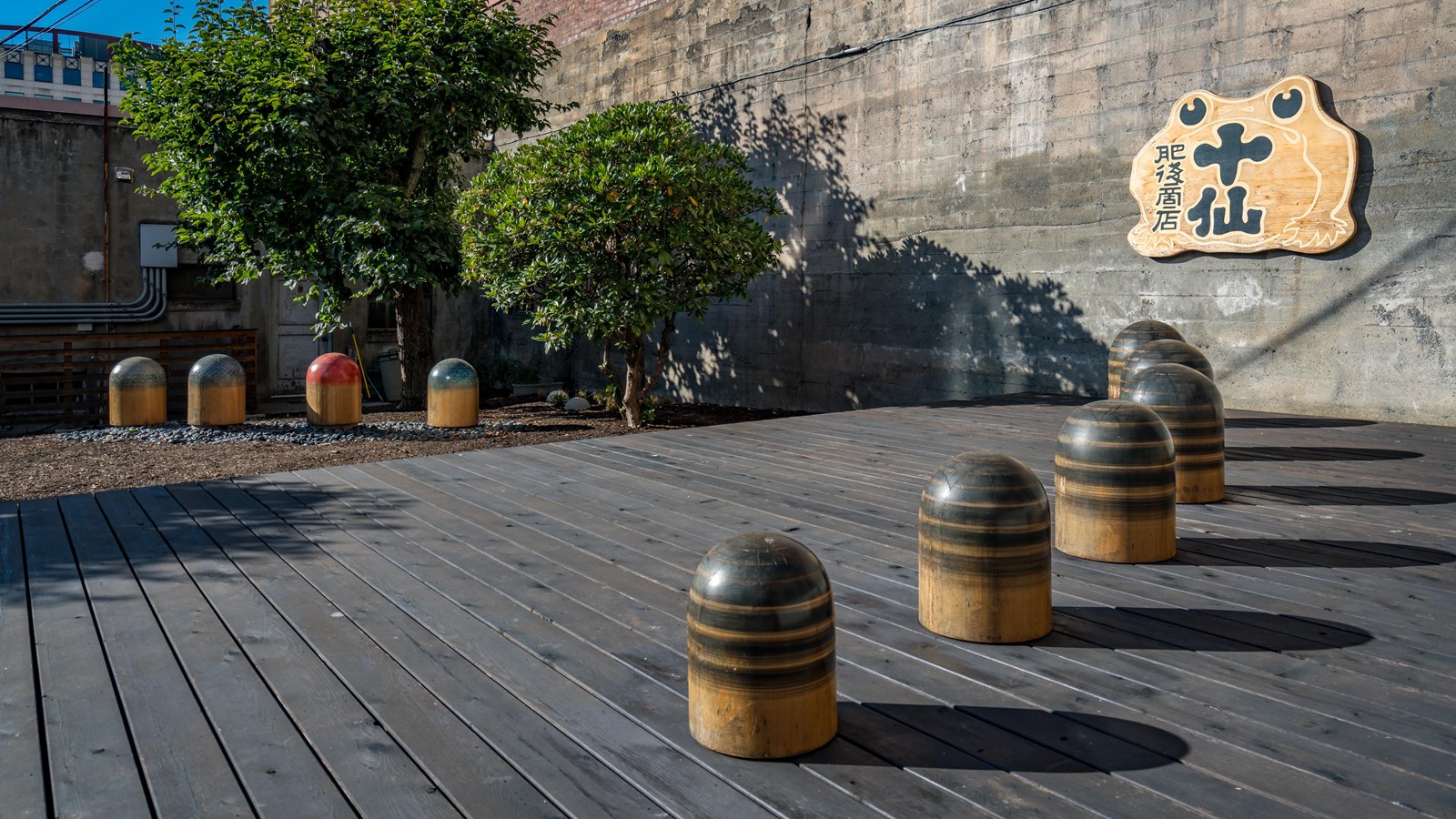 Sequence of large cylindrical objects on a wooden platform, with urban and natural elements.