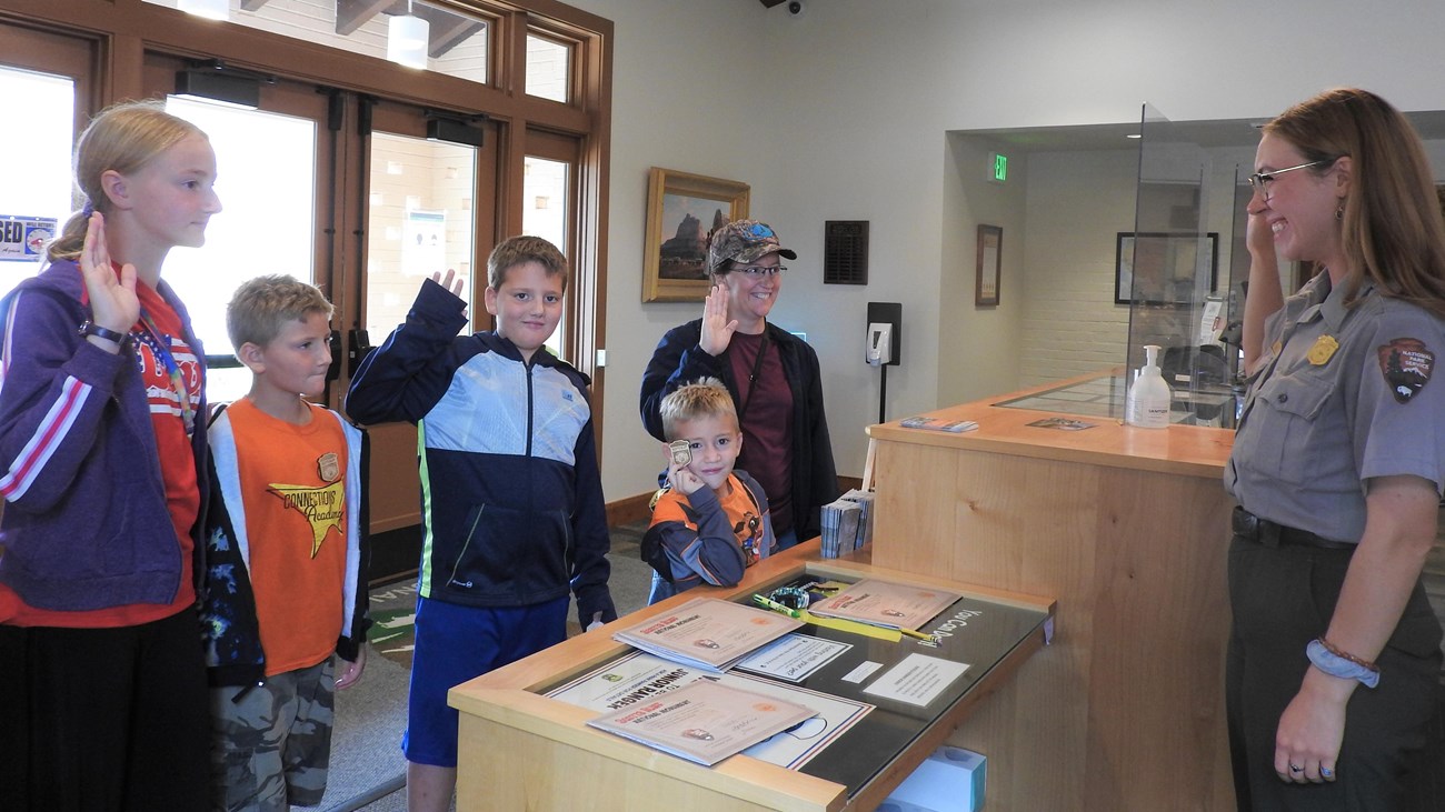 Five junior rangers raise their right hands and take the Junior Ranger Pledge with a NPS Ranger. 