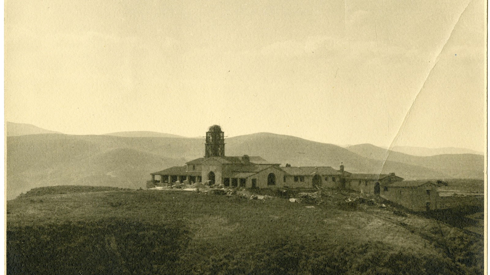 Black and white of large home on top of hill with other hills in the distance 
