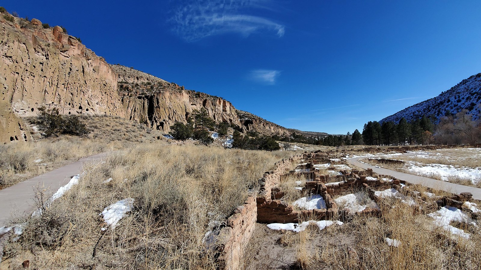 remnants of stone dwellings in the forefront and tan cliffs in the background with a bright blue sky