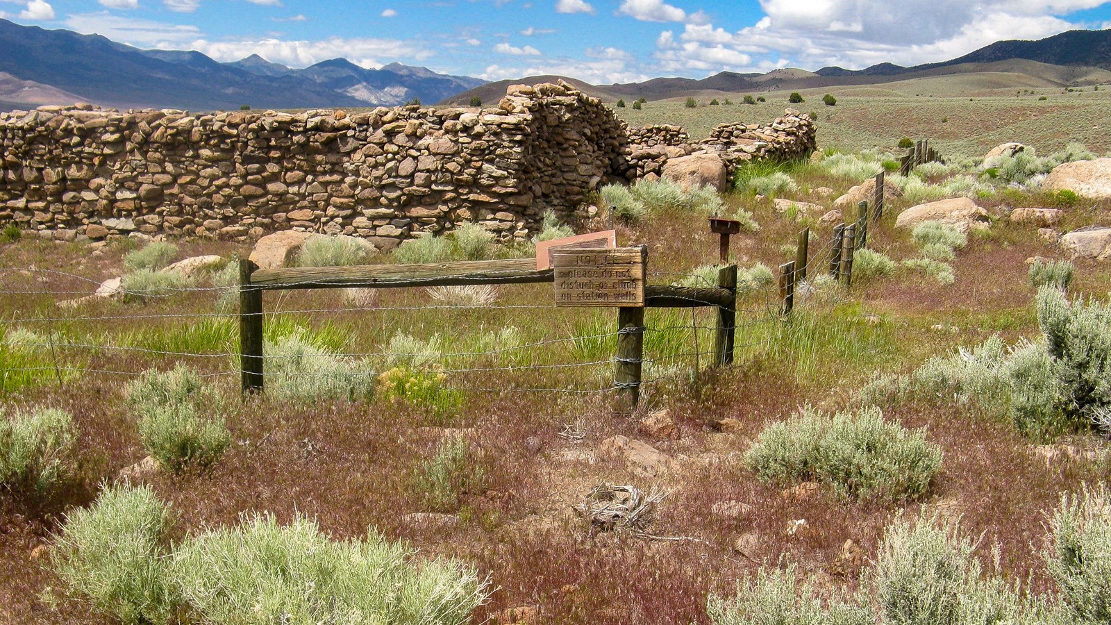 Standing stacked rock wall ruins of a building in a natural setting of sagebrush and mountains.