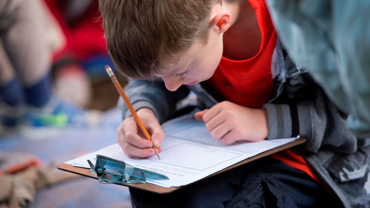 A kid works on a paper attached to a clipboard.