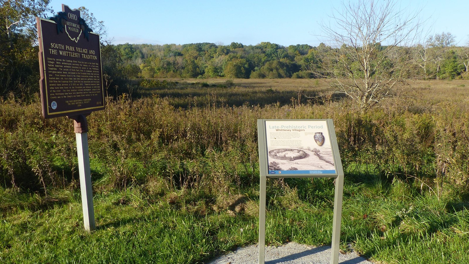 The historical marker is left of the panel. They overlook a meadow with a forested valley wall.