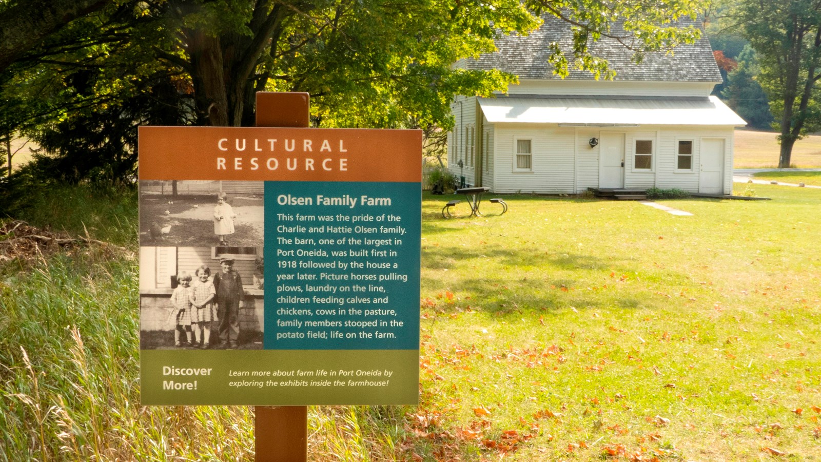 Sign with historic photo and text with bright light green field behind and white farmhouse behind