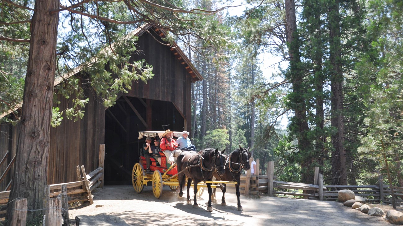 A stage drawn by two horses outside a covered bridge