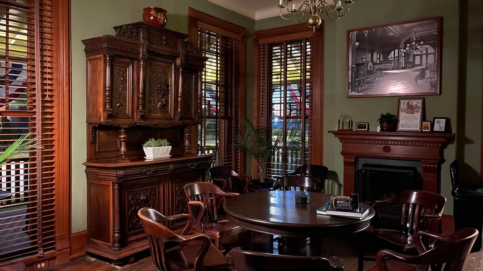 A Victorian styled living room with wooden furniture including a table, a cabinet, and a fireplace.