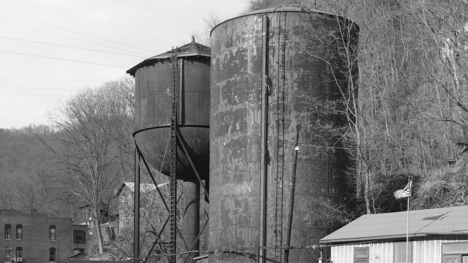Two large steel water tanks one a tall column and one elevated sitting next to railroad tracks