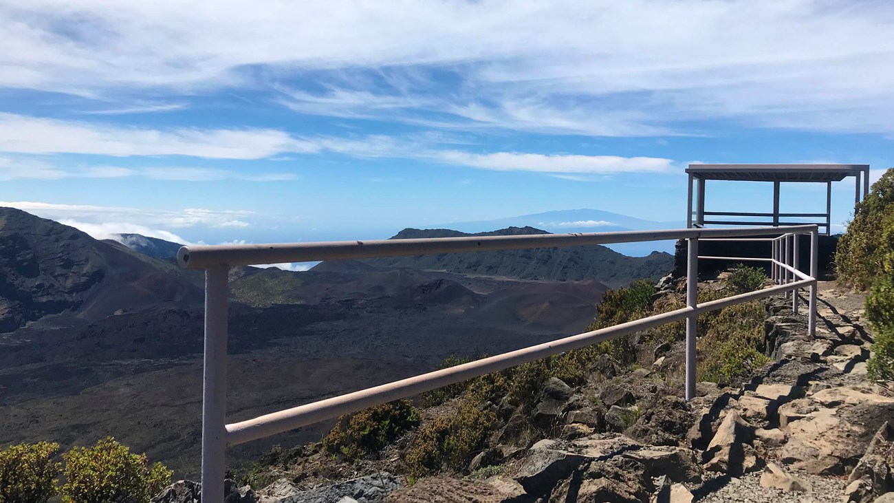 A path with a railing leads to an overlook next to a deep volcanic valley