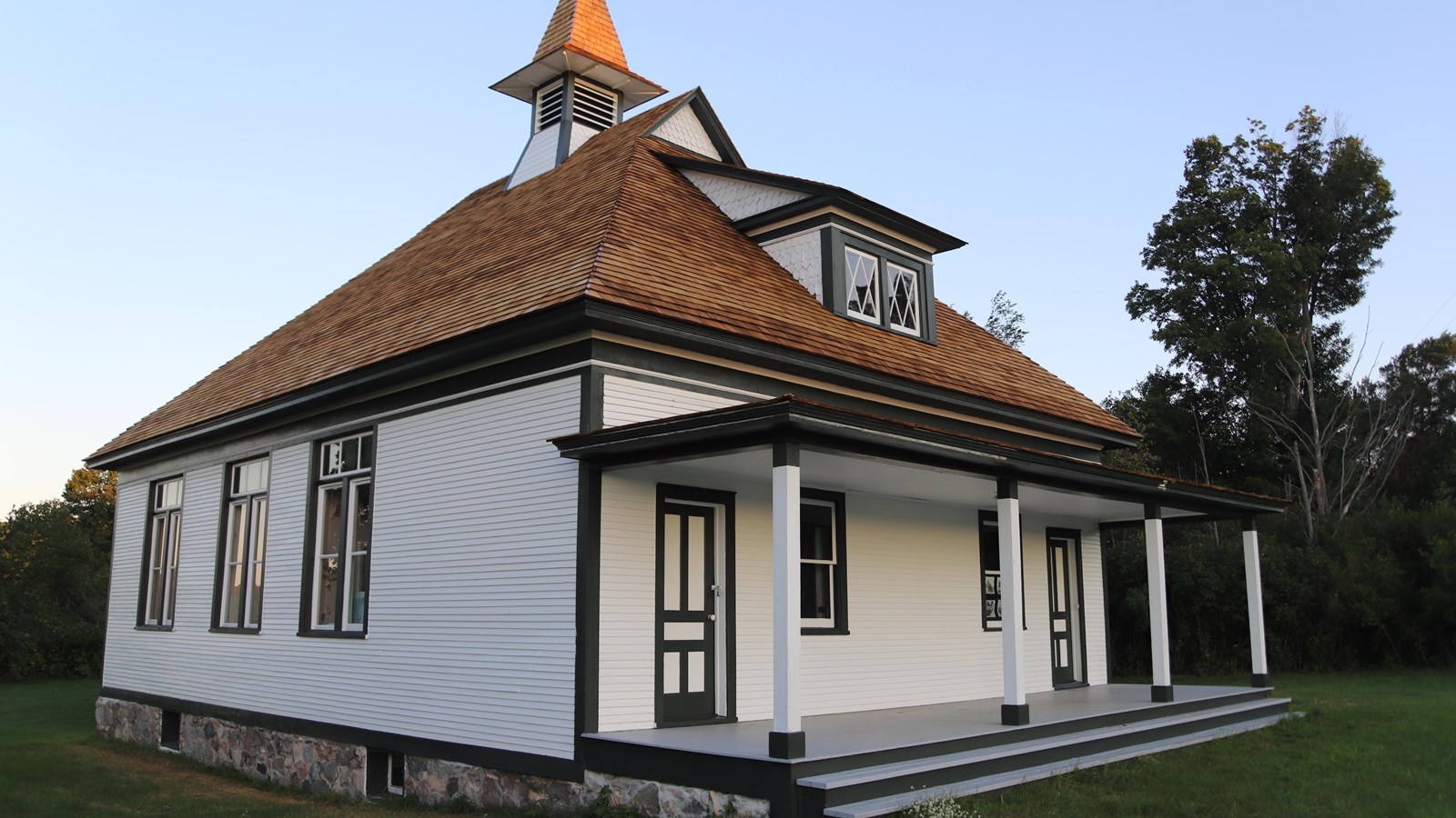 A white two-story schoolhouse with a brown roof. There are two entrance doors on the porch.