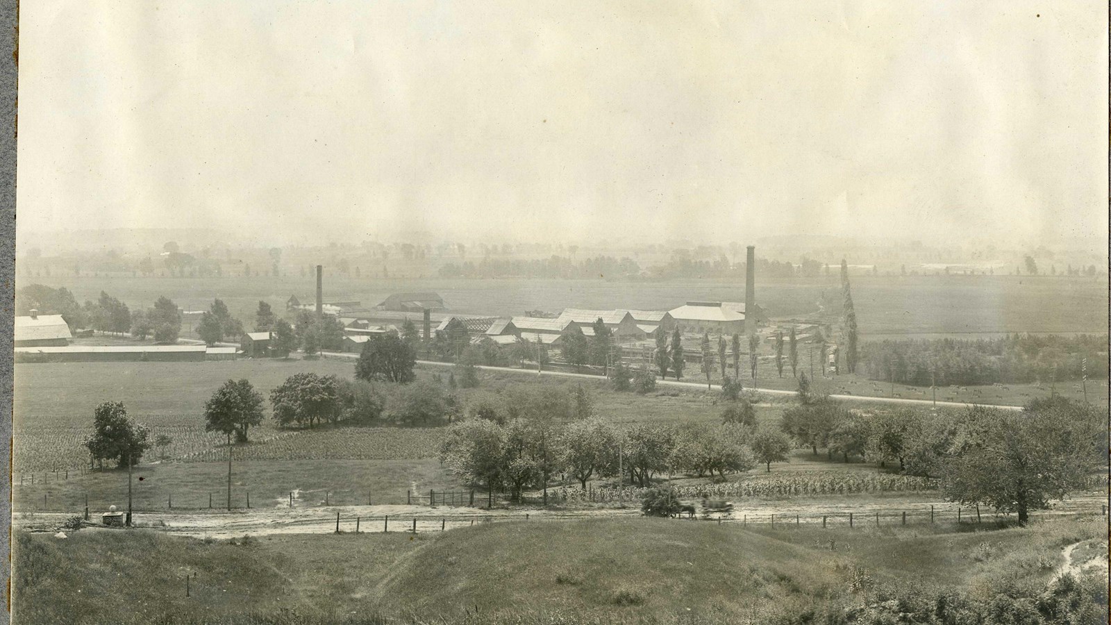 Black and white of large area of grass with trees along the roads, homes on roads