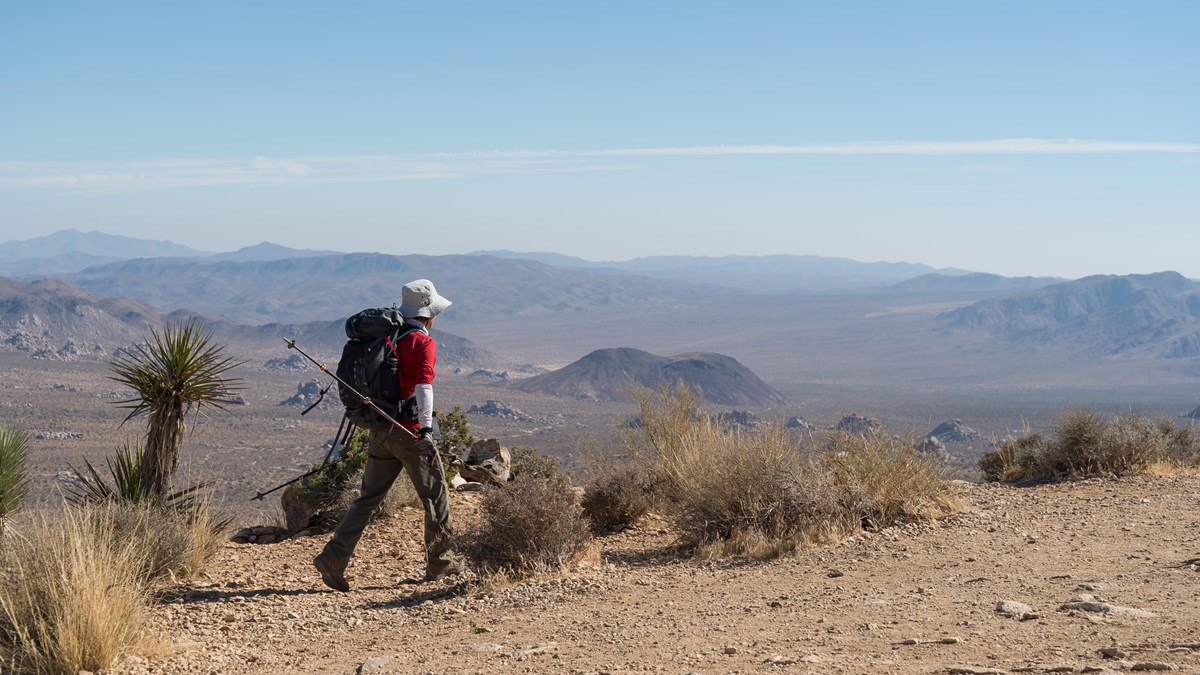 A person hiking a dirt trail on a mountain with mountains in the distance.
