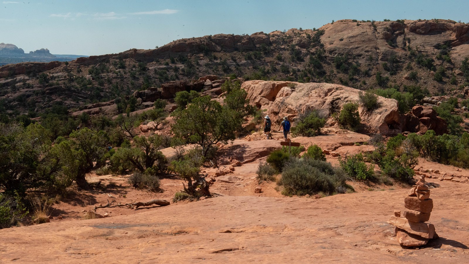 Stacked rocks guide two hikers across sandstone and juniper trees
