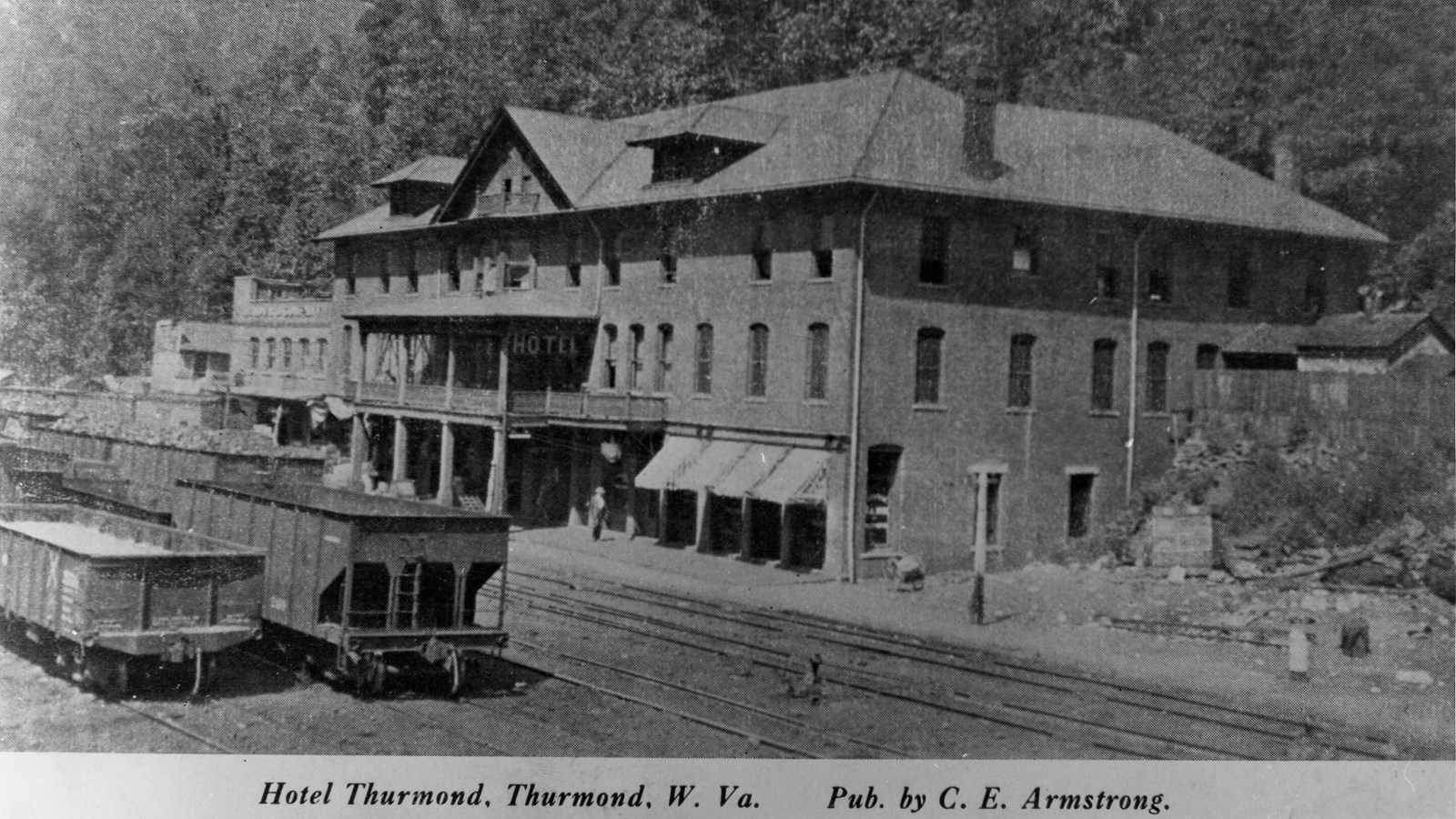 A large four story building with a veranda out front right next to railroad tracks.