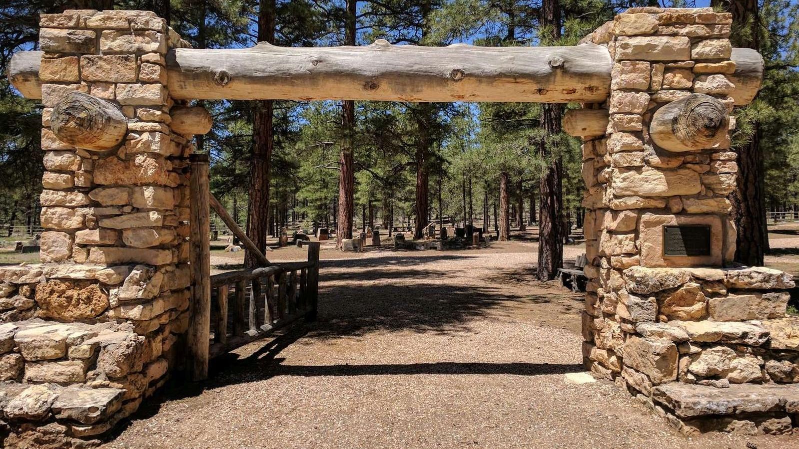 Two large white stone columns with a thick wooden beam stretching between frame a gravel path. 