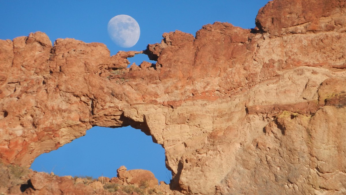 Two natural arches, stacked on top of each other, with the moon peeking out from behind.