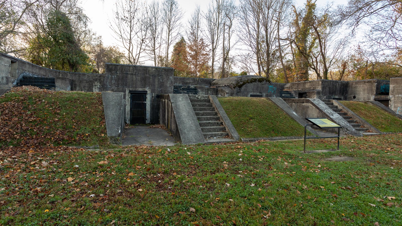A non-functioning building, low to the ground, is positioned in a field. Stairs lead up to it.