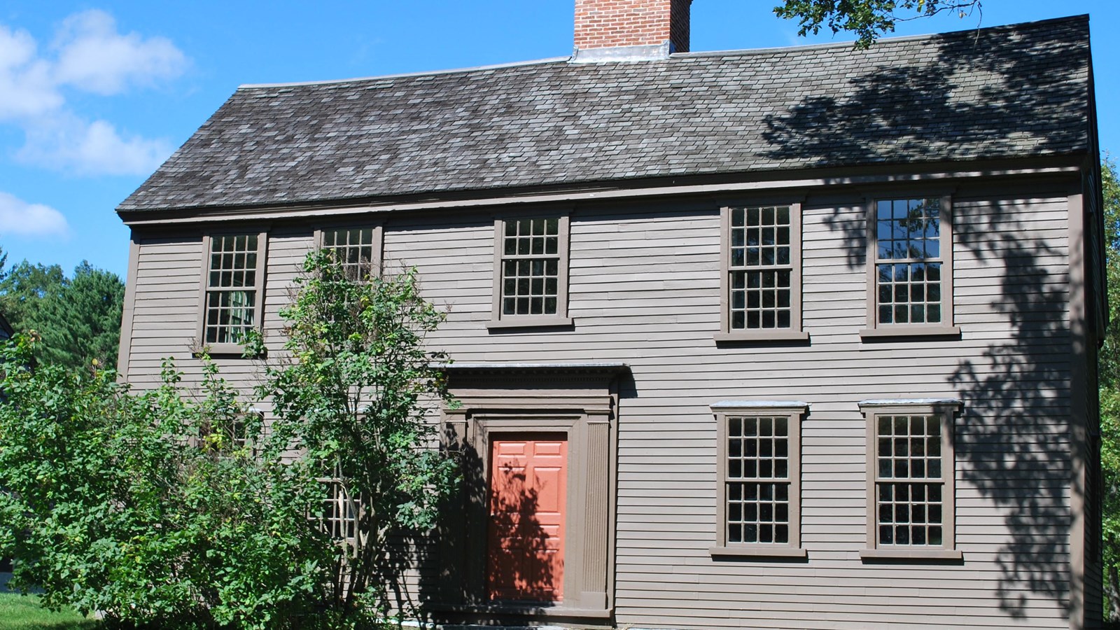 Two story wooden colonial house, dark brown wooden siding and a central chimney. 