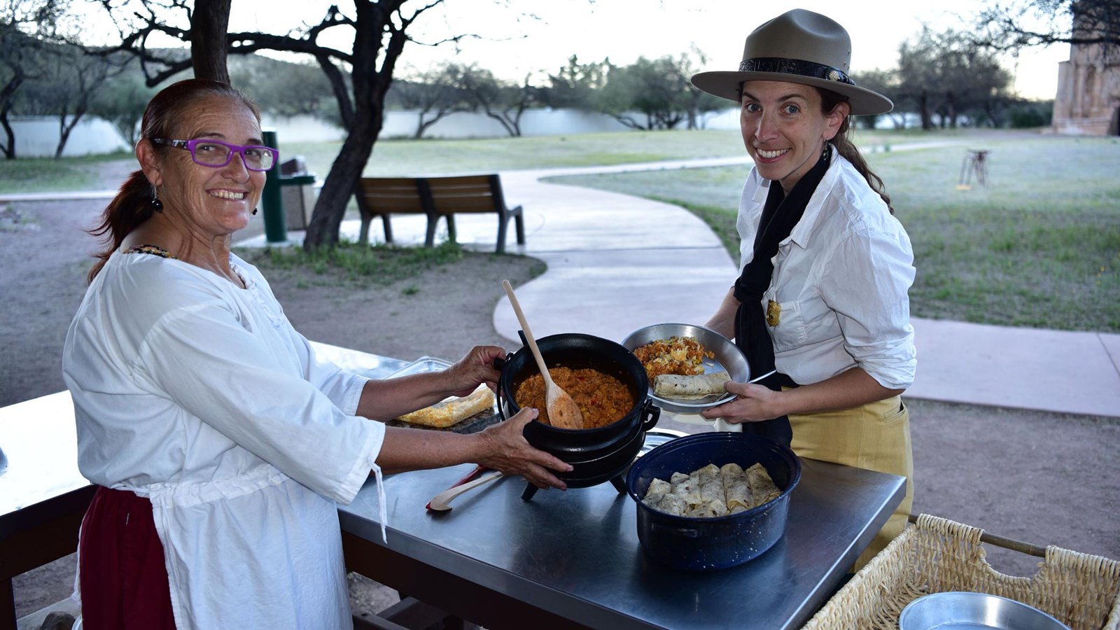 demonstrator and historically-costumed ranger pose with pot of stew
