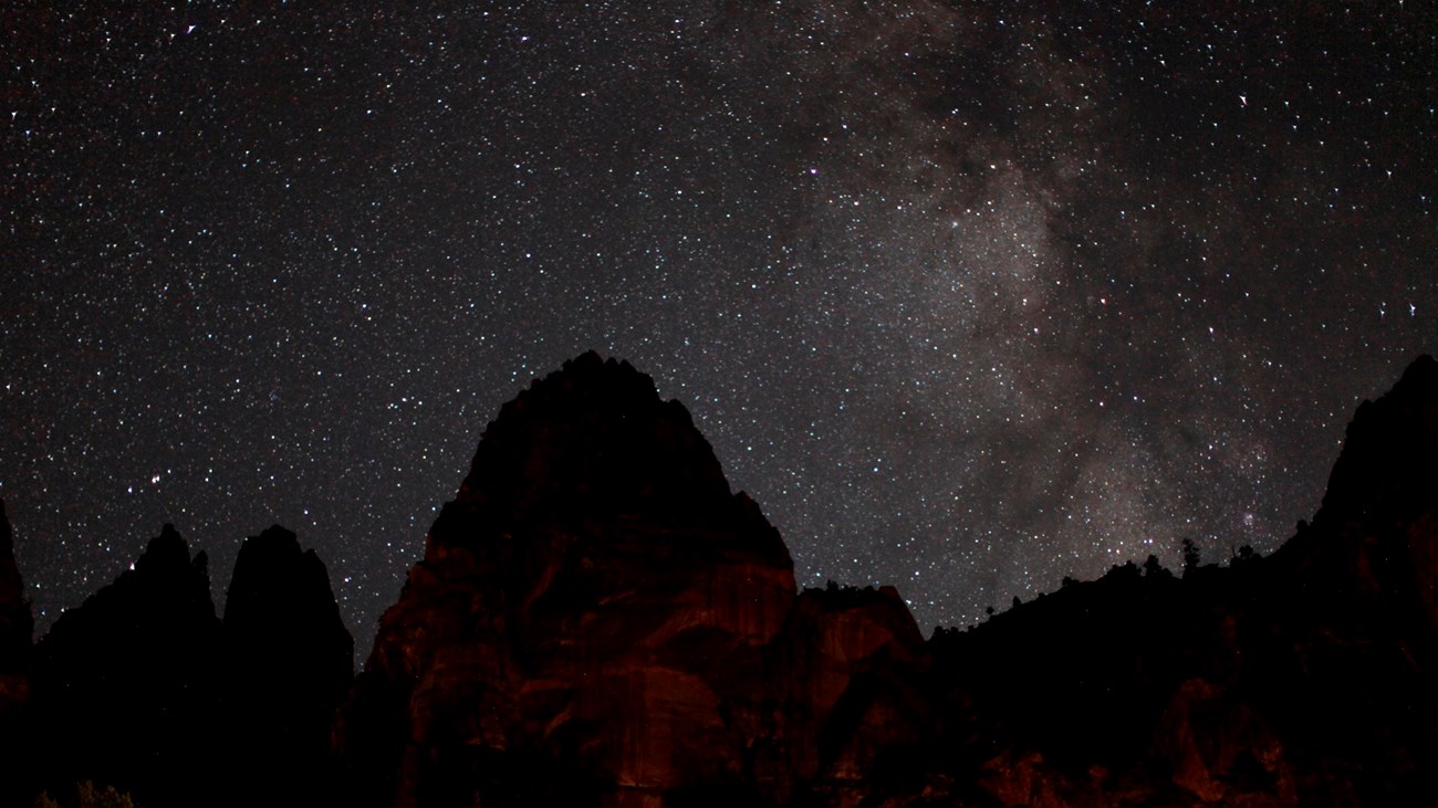 Black silhouette of a triangular mountain under a dark sky full of stars.