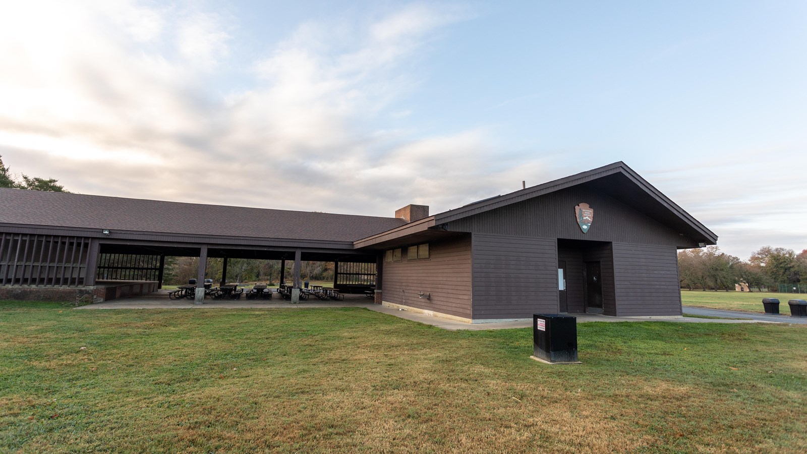 A building is connected to a picnic area with a roof and no walls.