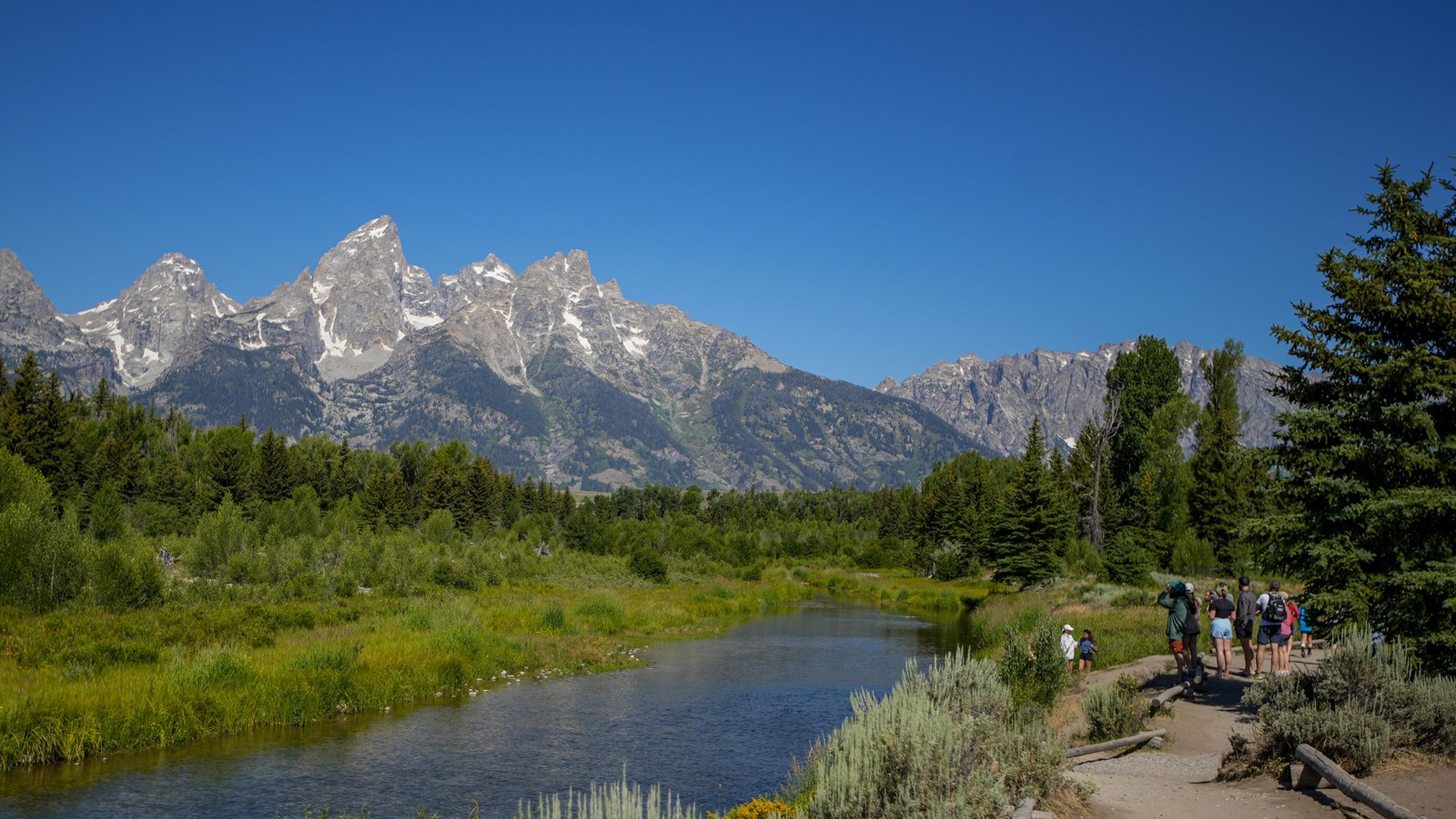 The teton range with a channel of the river flowing in front with people taking pictures. 
