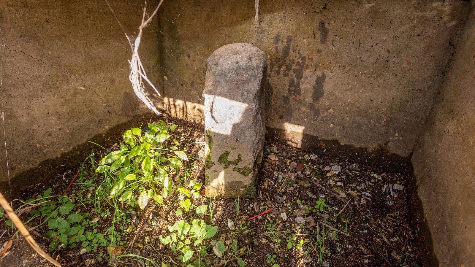A short, skinny-ish stone is positioned under a concrete box-like structure.