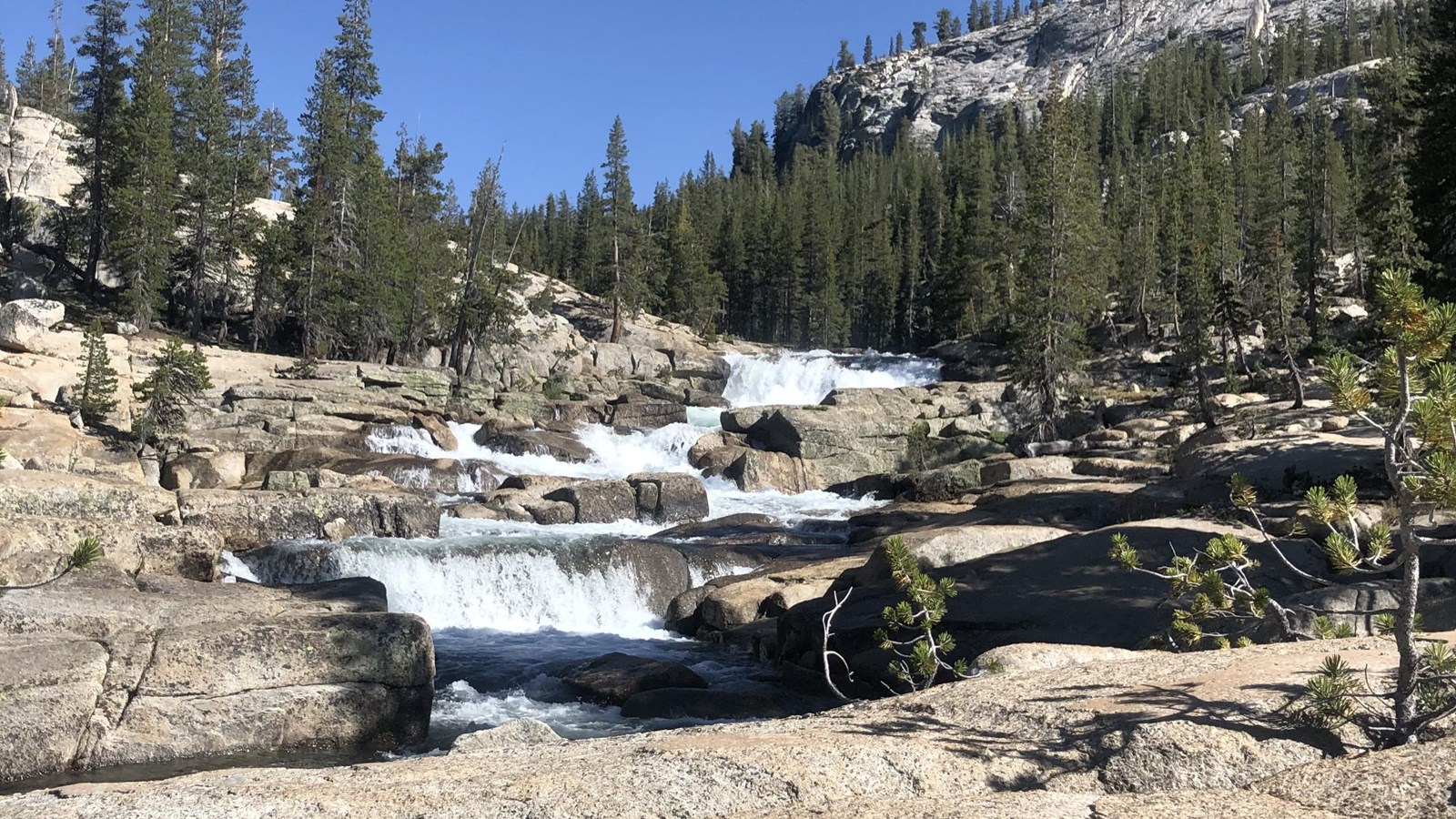 A river cascades over a series of short drops on bare granite