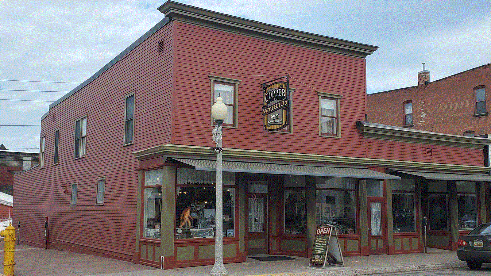 Two story red sided building with flat roof and green trim. Sign above the entrance reads “Copper Wo