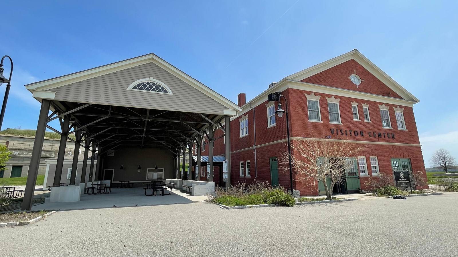 Sheltered pavilion with tables next to a three story rectangular brick building.