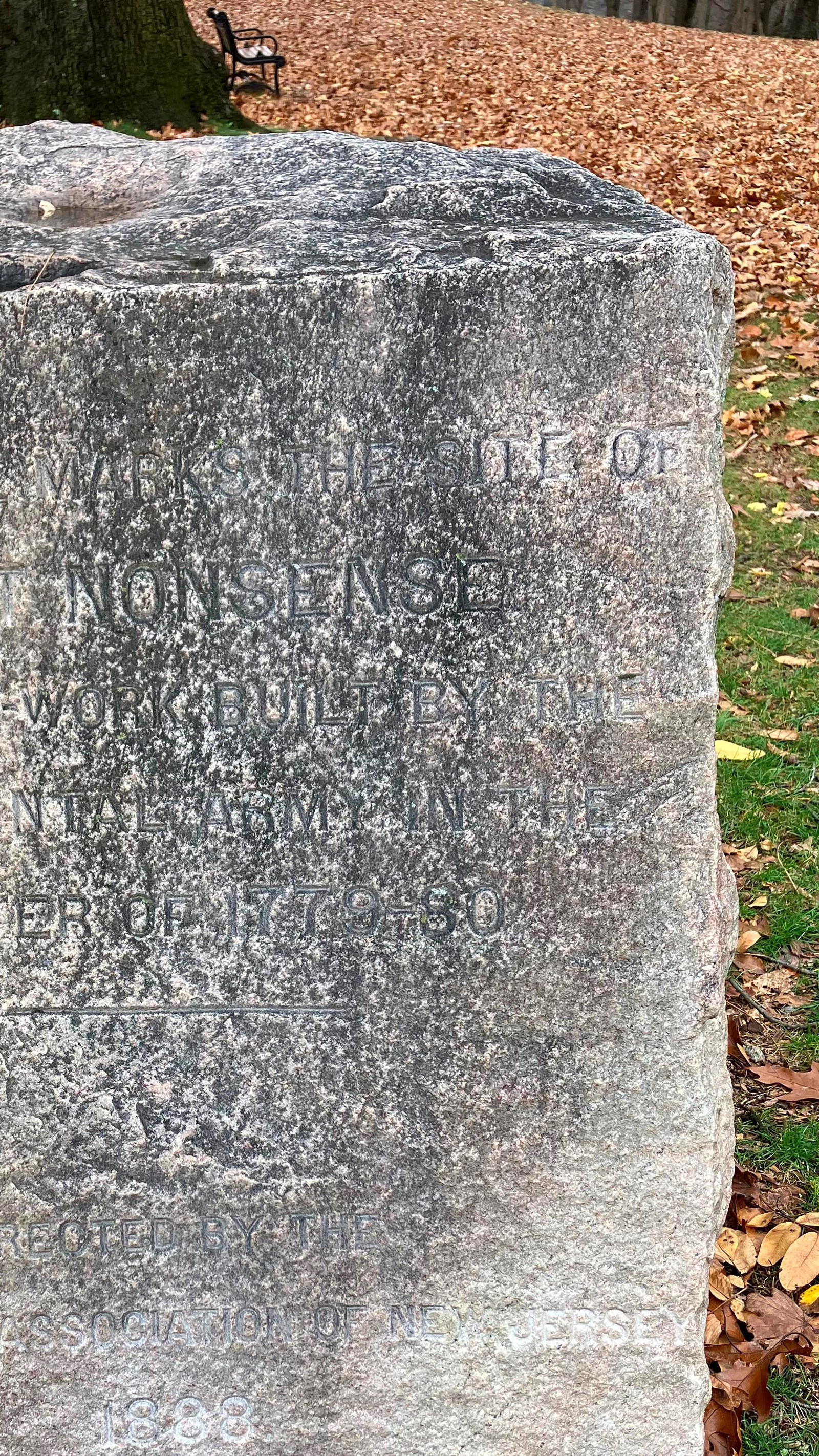 A large white stone weathered by exposure to elements with a memorial inscribed in it.
