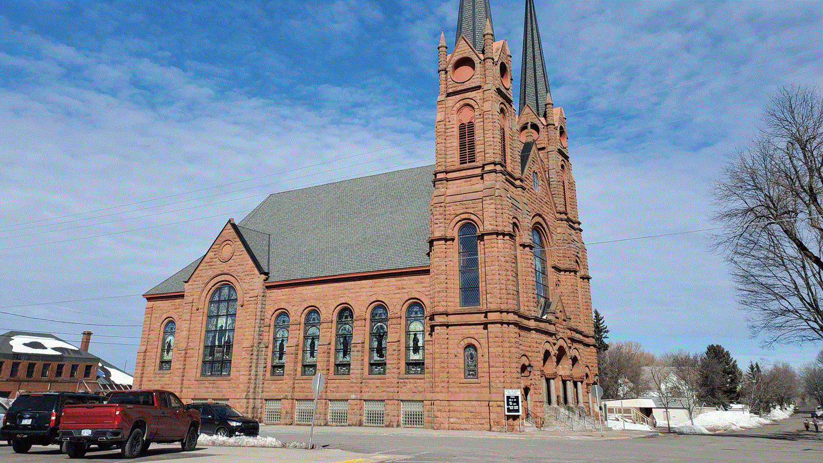 Tall red sandstone church with two spires and many arch-topped stained-glass windows.