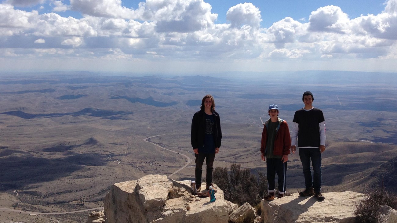 Three people stand on the summit of a mountain peak