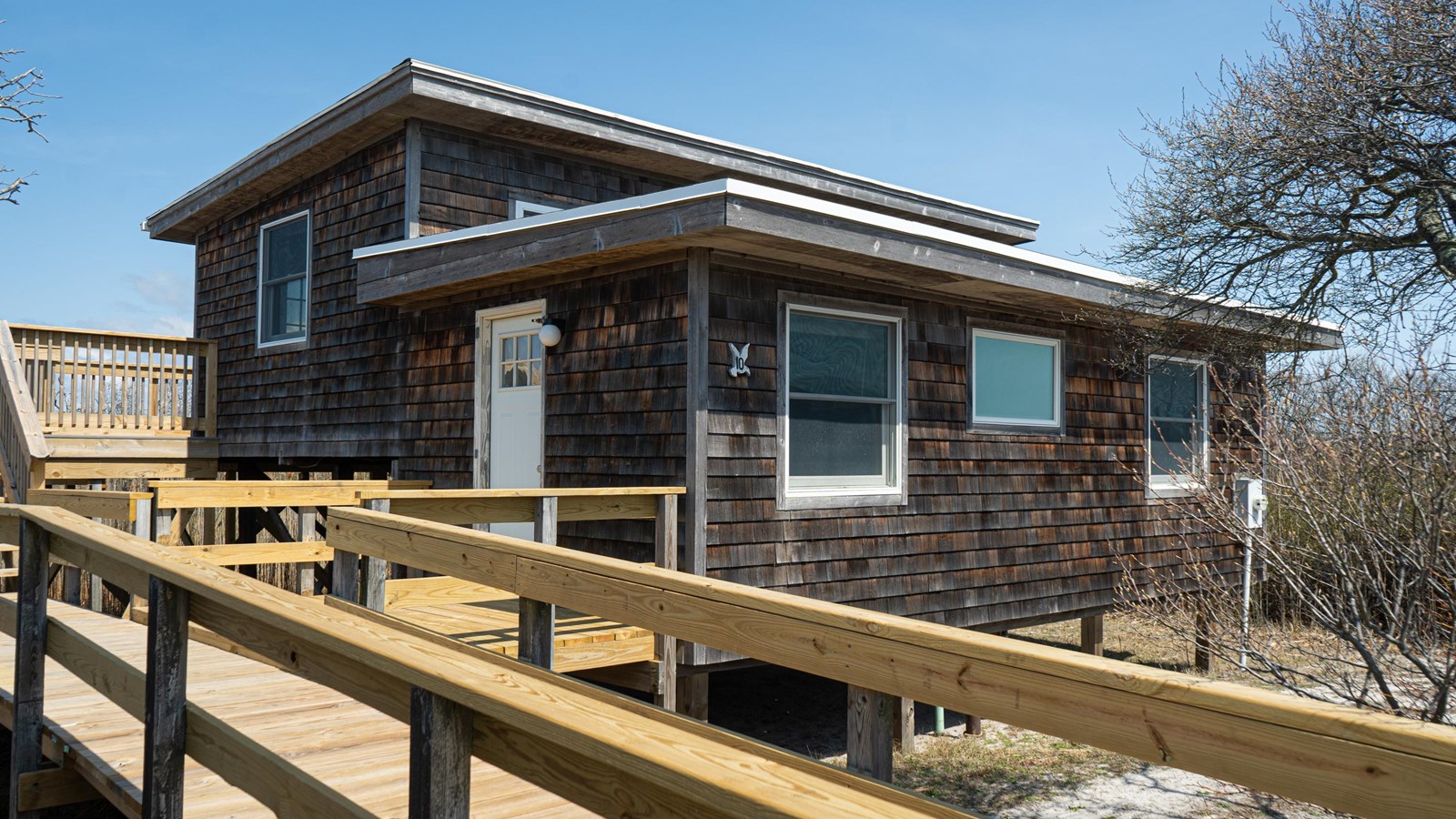 A wood-shingled raised beach house with surrounding decking.