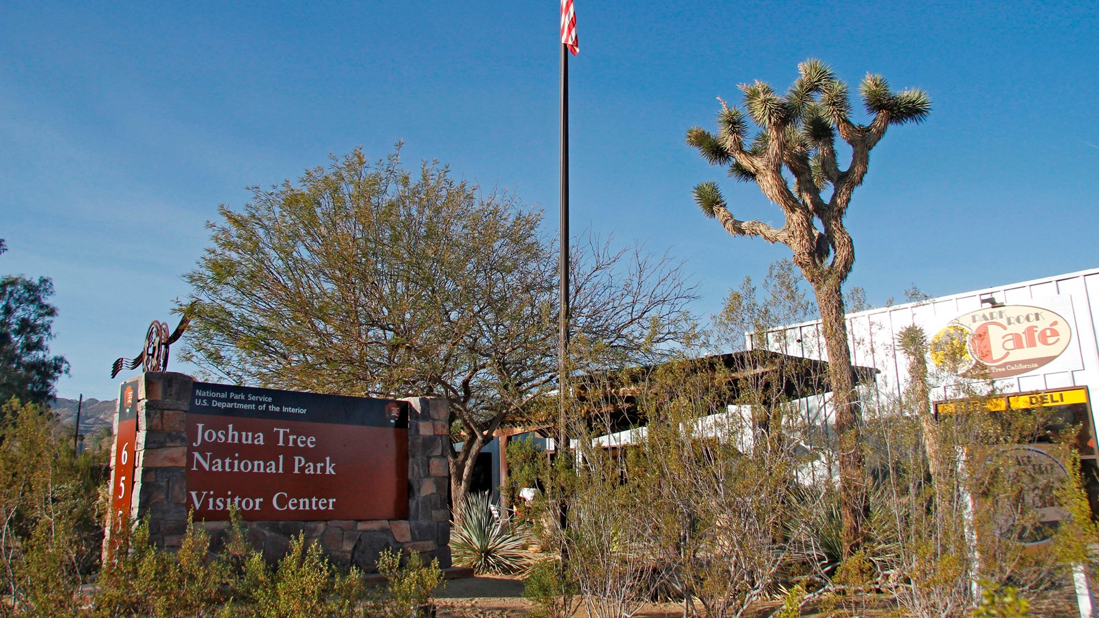 A gray building behind a flag pole and vegetation. There is a sign for