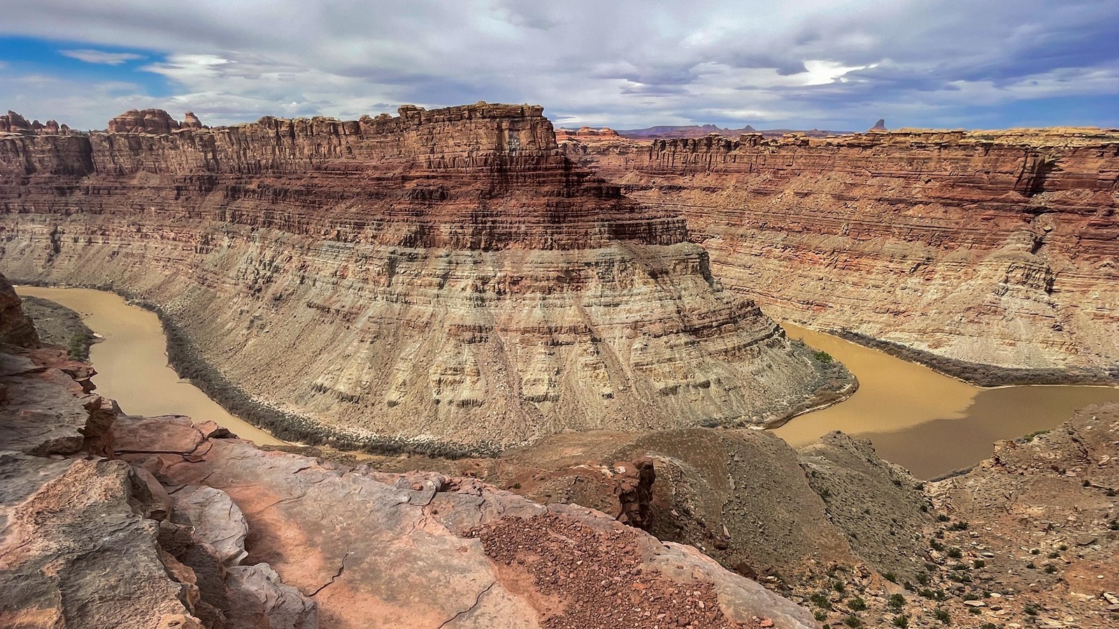 A green and gray river converge below towering canyon walls