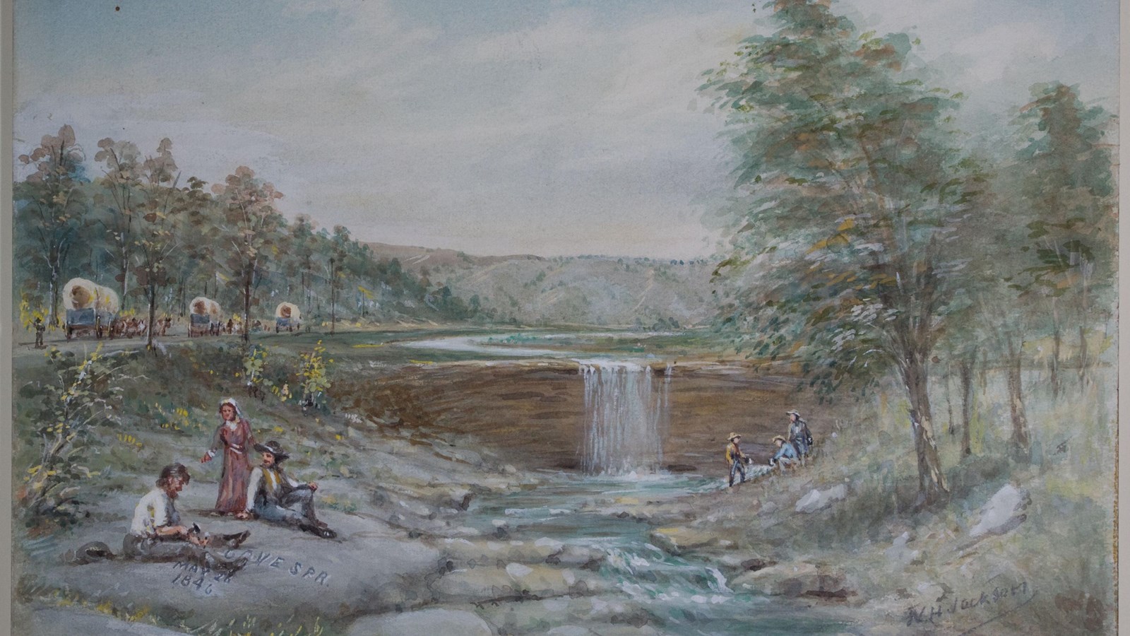 A wagon train near a small, rocky creek and waterfall the drops over a small cliff. 